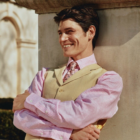 Man leaning on London monument in a pink linen shirt, sand coloured linen waistcoat and Cordings tie